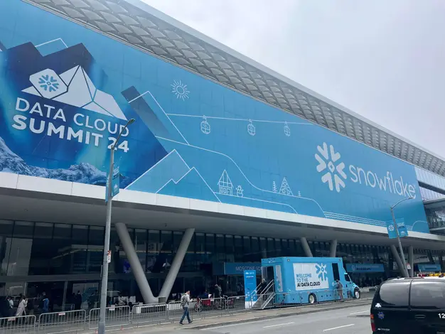 A large building displays a "Snowflake" logo and "Data Cloud Summit 2024" on the front of the building. A branded truck and attendees are visible below. The design includes mountain and gondola graphics.